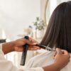 Close-up of a hairstylist's hands trimming a client's hair with scissors and comb at a salon, soft neutral background