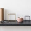 Console table styled with a roll of kraft paper, hair scissors, and wire cubes holding a small blush cosmetic jar