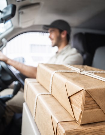 Delivery driver in a van with a wrapped beauty product parcel on the dashboard-side seat