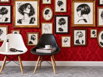 Salon styling corner with two chairs in front of a bold red patterned feature wall decorated with framed black and white