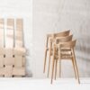 Stack of three light wooden salon chairs beside a woven wood-panel wall display in a bright salon