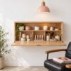 Wall-mounted wooden beauty vanity cabinet opened to show unbranded skincare and nail products, with blush pendant lamp