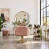 Wide view of a bright airy hair salon interior with a styling chair, mirror and blush-pink accents
