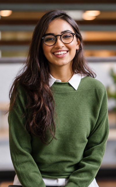 Smiling young South African Indian female legal associate with glasses in a green knit jumper over a white collar